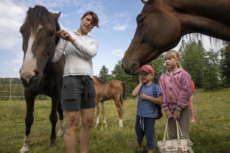 Viljakukka Lähteenmäki tyttönsä ja poikansa kanssa hevosten keskellä. Kaksi ruskeaa hevosta ja vaaleanruskea varsa.