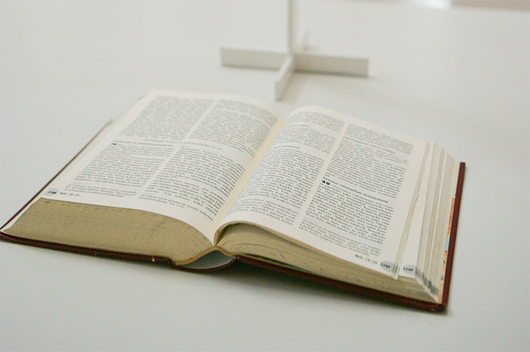 Arkinen ja hieman kulunut Raamattu on asetettu alttarille, valkoisen puuristin juurelle.