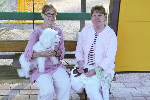 Kaksi naista istuu penkillä, vasemmanpuoleisen naisen sylissä on koira.