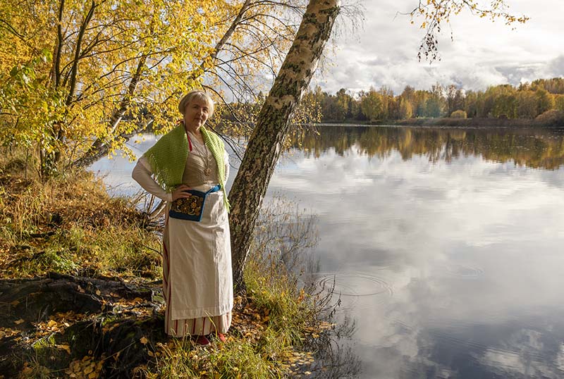 Nainen syksyisessä maisemassa järven rannalla puun vieressä.