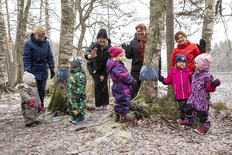 Lapsia ja aikuisia leikkii talvisella rannalla puiden lomassa.