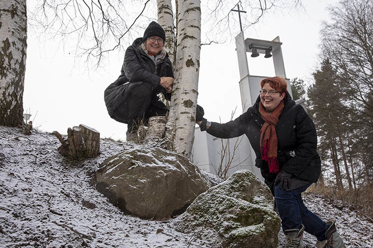 Kaksi naista lumisessa rinteessä ja taustalla kirkon kellotapuli.