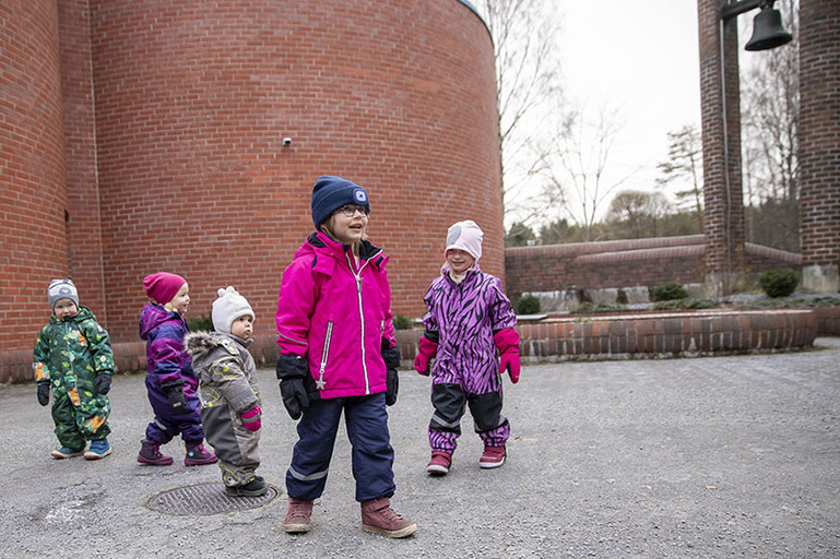 Lapsia tiilivuoratun kirkon pihalla, kirkontorni näkyy taustalla.