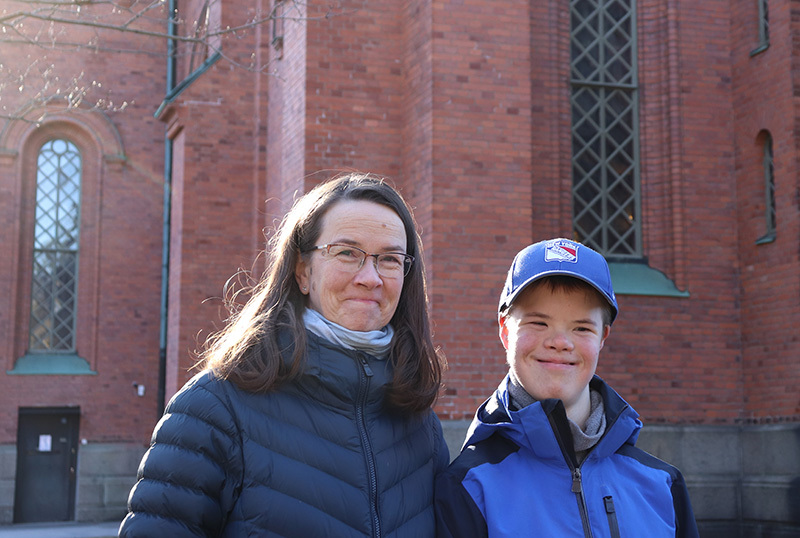 Poika ja äiti hymyilevät aurinkoisessa säässä kirkon edessä.