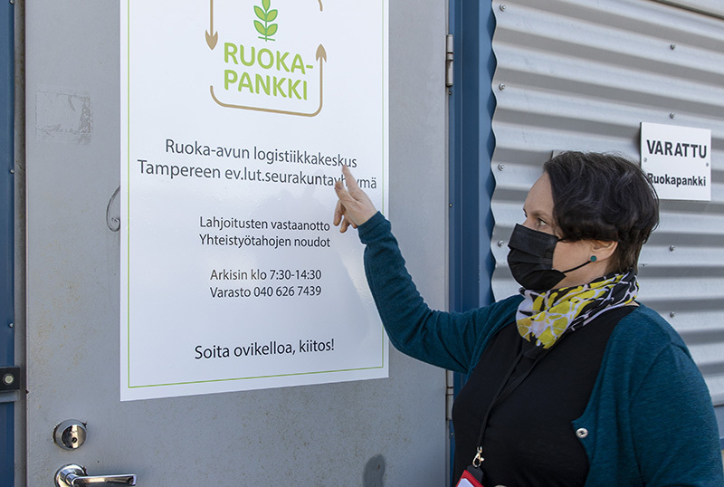 Nainen seisoo ruokapankin ovella ja osoittaa info-tekstejä.