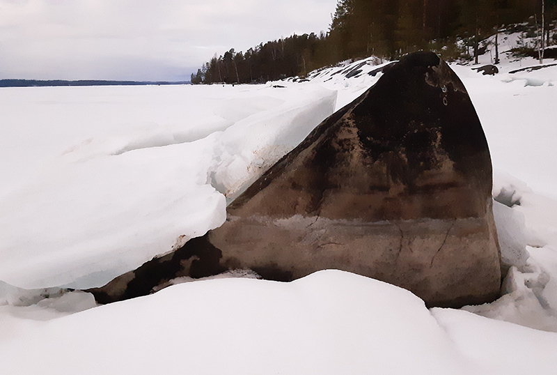 Iso lohkare murtuneiden jäiden keskellä rannalla.