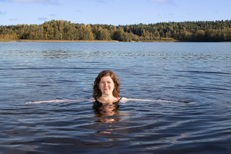 Nainen veden keskellä. Vain pää näkyy, ja levitetyt kädet kuultavat veden läpi.