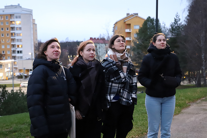 Neljä nuorta naista seisoo vierekkäin lämpimästi pukeutuneena ulkona.