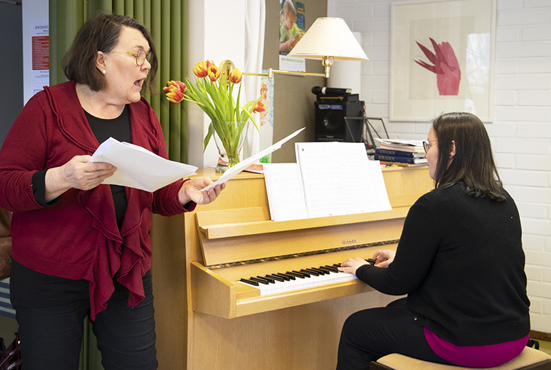 Nainen laulaa eläytyen, ja toinen soittaa vieressä pianoa.