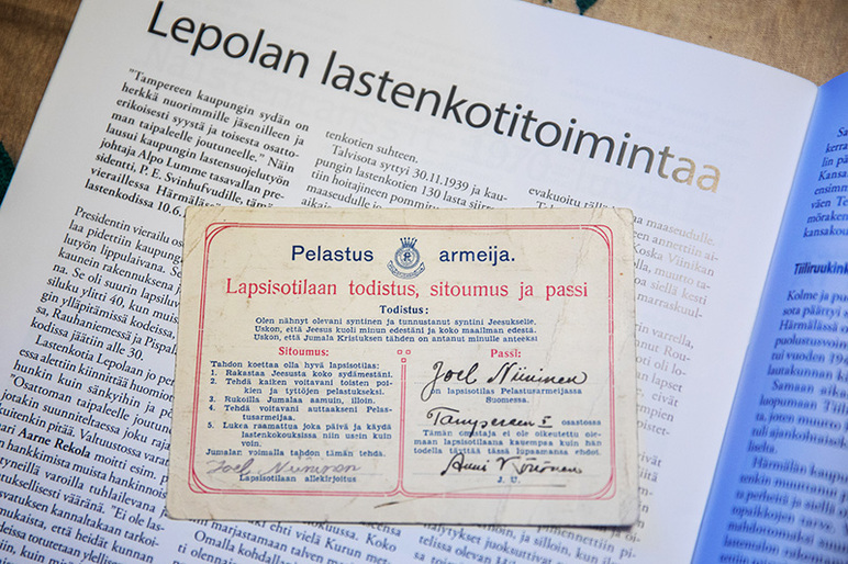 Lehtiaukeaman päällä on paperi, jossa lukee muun muassa "Pelastus armeija. Lapsisotilaan todistus, sitoumus ja passi"