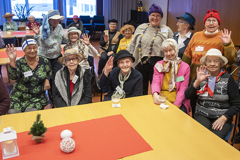 Pöydän taakse on ryhmittynyt iloista väkeä, joilla kaikilla on päähine.