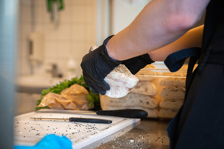 Kädet repivät leipää kahtia leikkuulaudan yläpuolella. Leikkuulaudalla on kaksi leikkuuveistä.