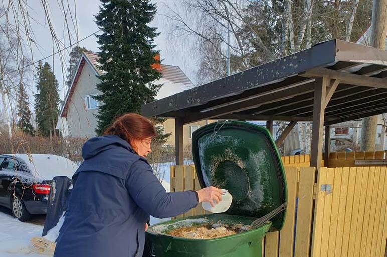 Henkilö laittaa lisää jätettä kompostiin talvella.