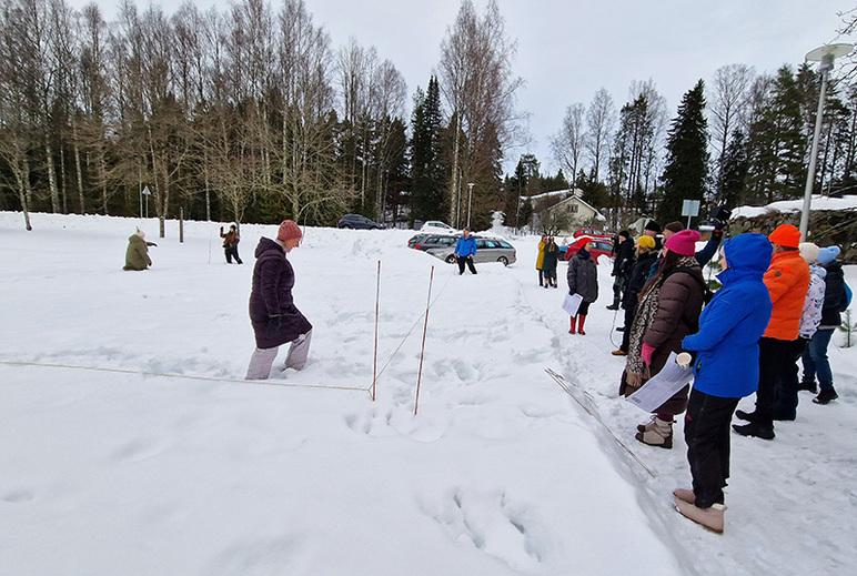Muutamia ihmisiä kahlaa lumessa narujen keskellä, ja muut seisovat lumisella tiellä vieressä.