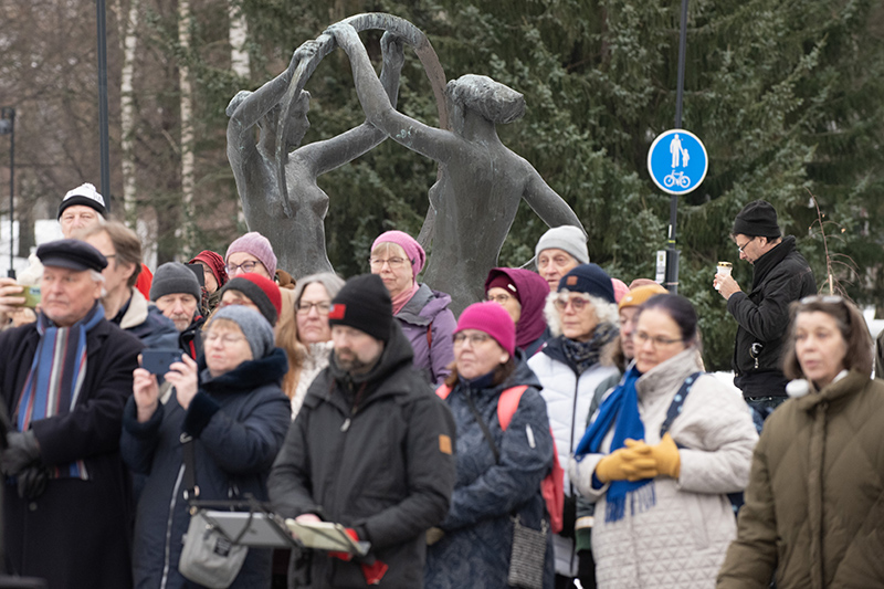 Iso joukko ihmisiä patsaan edessä, heistä osa rukoilee ja joku ottaa kuvia matkapuhelimella.